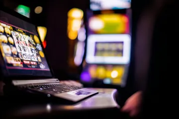 A woman smiling by bright slot machines showing lucky symbols, showcasing the exciting slot offerings at LEGIONBED.